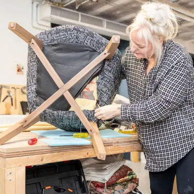 Student werkt nauwkeurig aan het restaureren van een houten stoel in een praktijkleeromgeving voor meubelbouw