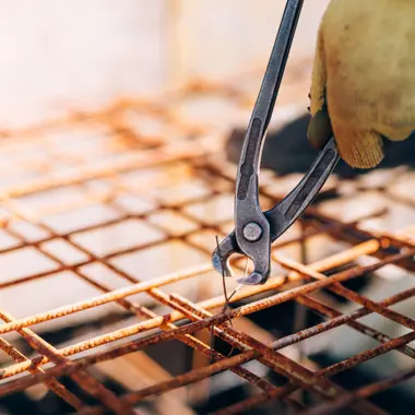 Vakman gebruikt tang om verbindingen in betonwapening op een bouwplaats te bevestigen