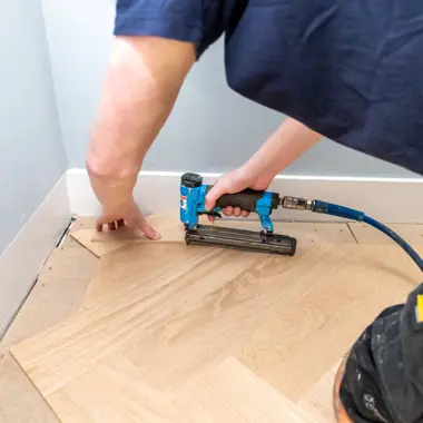 Vakman bevestigt parketvloer aan de rand van een kamer met een spijkerpistool