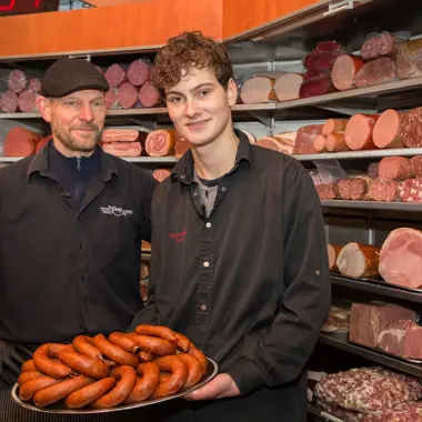 Twee ambachtelijke worstmakers presenteren vers bereide worsten in een traditionele slagerij.
