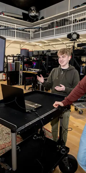 Twee studenten bespreken cameratechniek bij een monitor in een studio met professionele apparatuur
