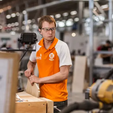 Leerling houtbewerking werkt nauwkeurig aan meubelstuk in een werkplaats voor hout en meubel.