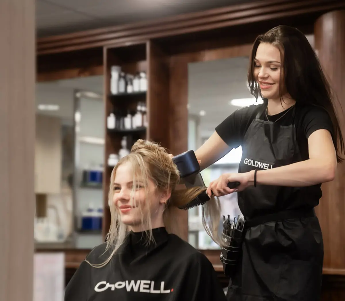 Leerling-kapper werkt in een salon en droogt haar van een klant als onderdeel van haar opleiding uiterlijke verzorging.
