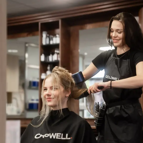 Leerling-kapper werkt in een salon en droogt haar van een klant als onderdeel van haar opleiding uiterlijke verzorging.