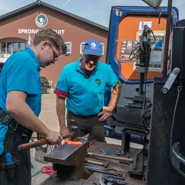 Leerling leert technieken van een vakman bij het beslaan van paardenhoeven buiten een smederij