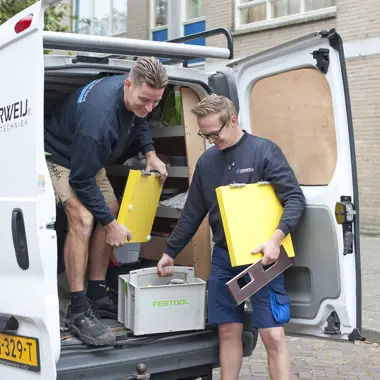 Montagemedewerkers laden gereedschapskisten in een werkbus voor houtbewerking en meubelmontage.