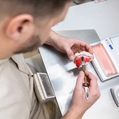 Student voert nauwkeurig tandtechnische handelingen uit aan een gebitsmodel in een werkplaats.