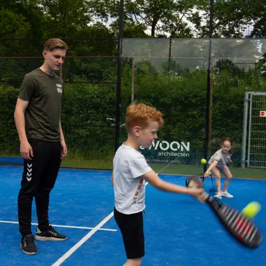 Begeleider geeft jonge sporter instructies tijdens tennisles op een sportveld