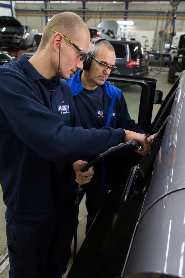 Twee autoschadeherstellers plaatsen een autoruit in een voertuig in een werkplaatsomgeving.