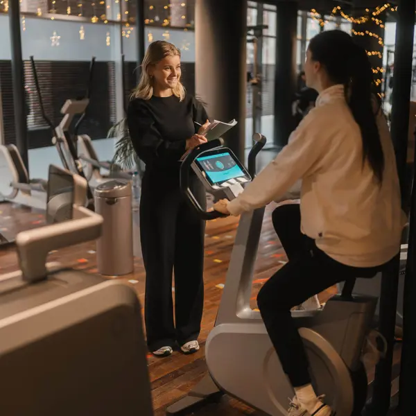 Studieloopbaanbegeleider en leerling bespreken trainingsschema in fitnesscentrum tijdens praktijkles voeding en leefstijladvies