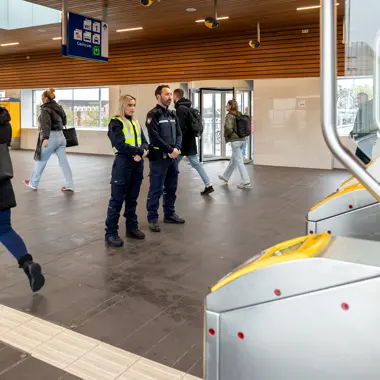 Toezichthouders controleren entree van openbaar vervoershal waar diverse reizigers lopen