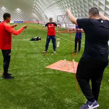 Groep jongeren oefent coördinatie en samenwerking tijdens een interactieve bewegingsactiviteit in een sporthal.
