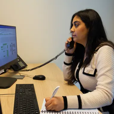 Medewerker in een kantooromgeving voert telefonisch overleg en maakt notities tijdens werk met computersysteem