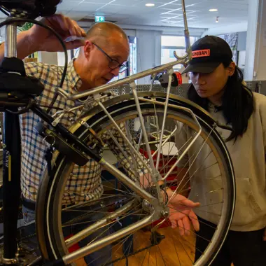 Assistent mobiliteitsbranche bespreekt fietsreparatie in werkplaats met kandidaat-student
