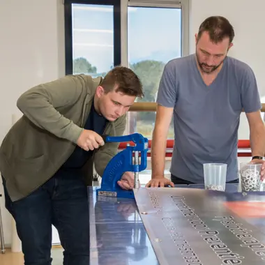 Twee studenten werken samen aan een groot vormgevingsproject met snijmachine in een creatieve leeromgeving