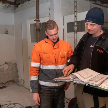 Twee bouwvakkers bekijken een bouwtekening in een hal onder constructie