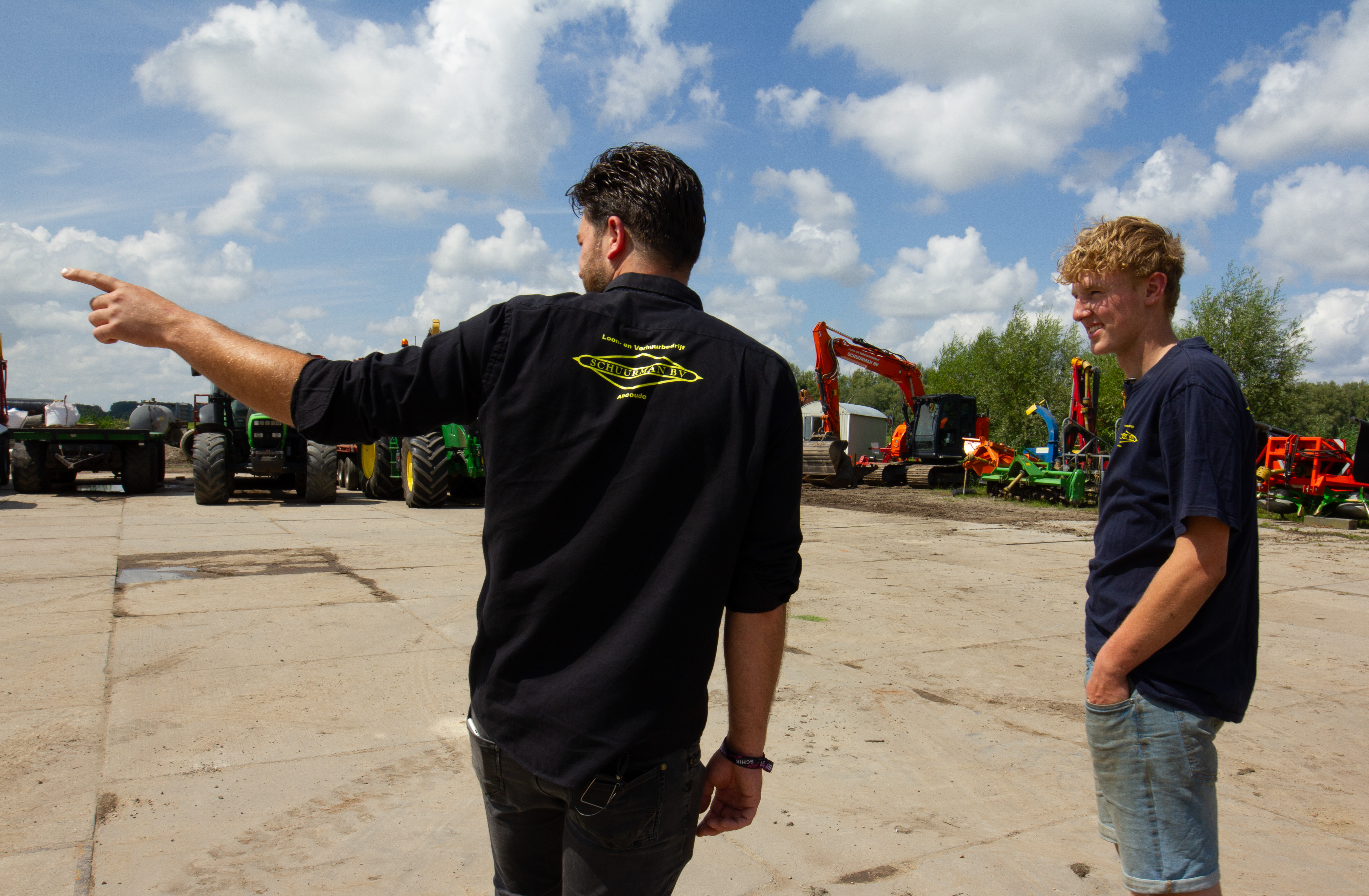 Twee jongeren bespreken buiten het gebruik van machines bij groenonderhoud en grondwerk in een werkplaats.