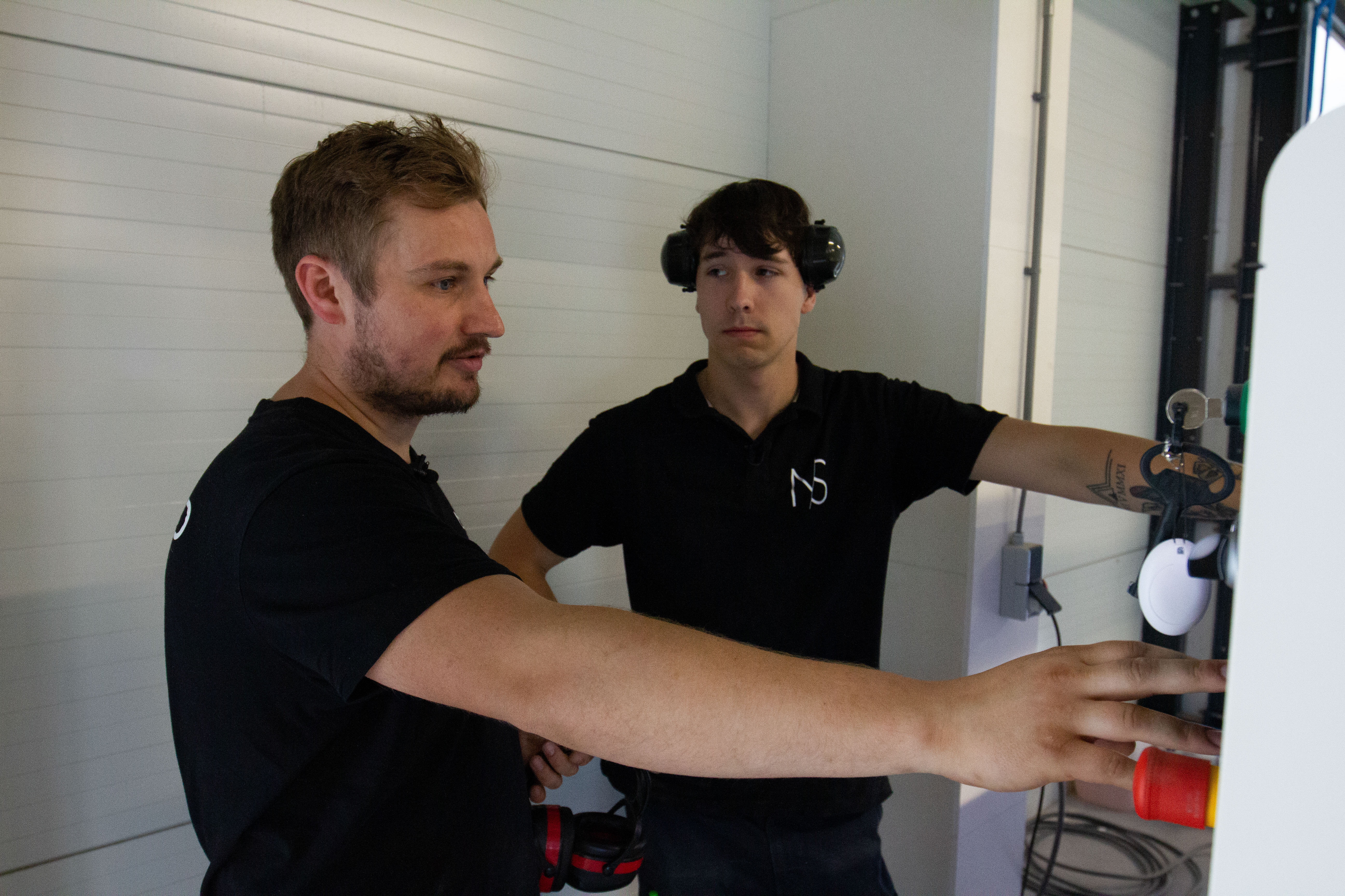 Twee vakbekwame meubelmakers bedienen en controleren een houtbewerkingsmachine in een werkplaats.