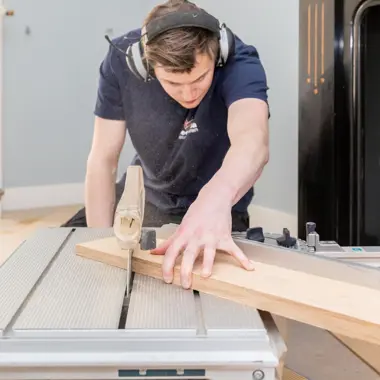 Student werkt met houtzaag om planken op maat te zagen voor interieurproject.