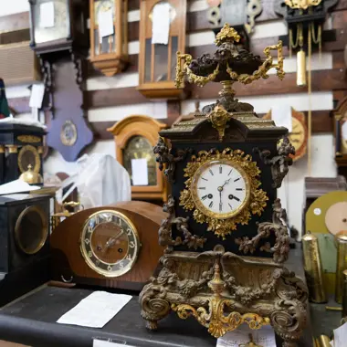 Klokkenmaker aan het werk te midden van verschillende antieke en klassieke uurwerken in een werkplaats