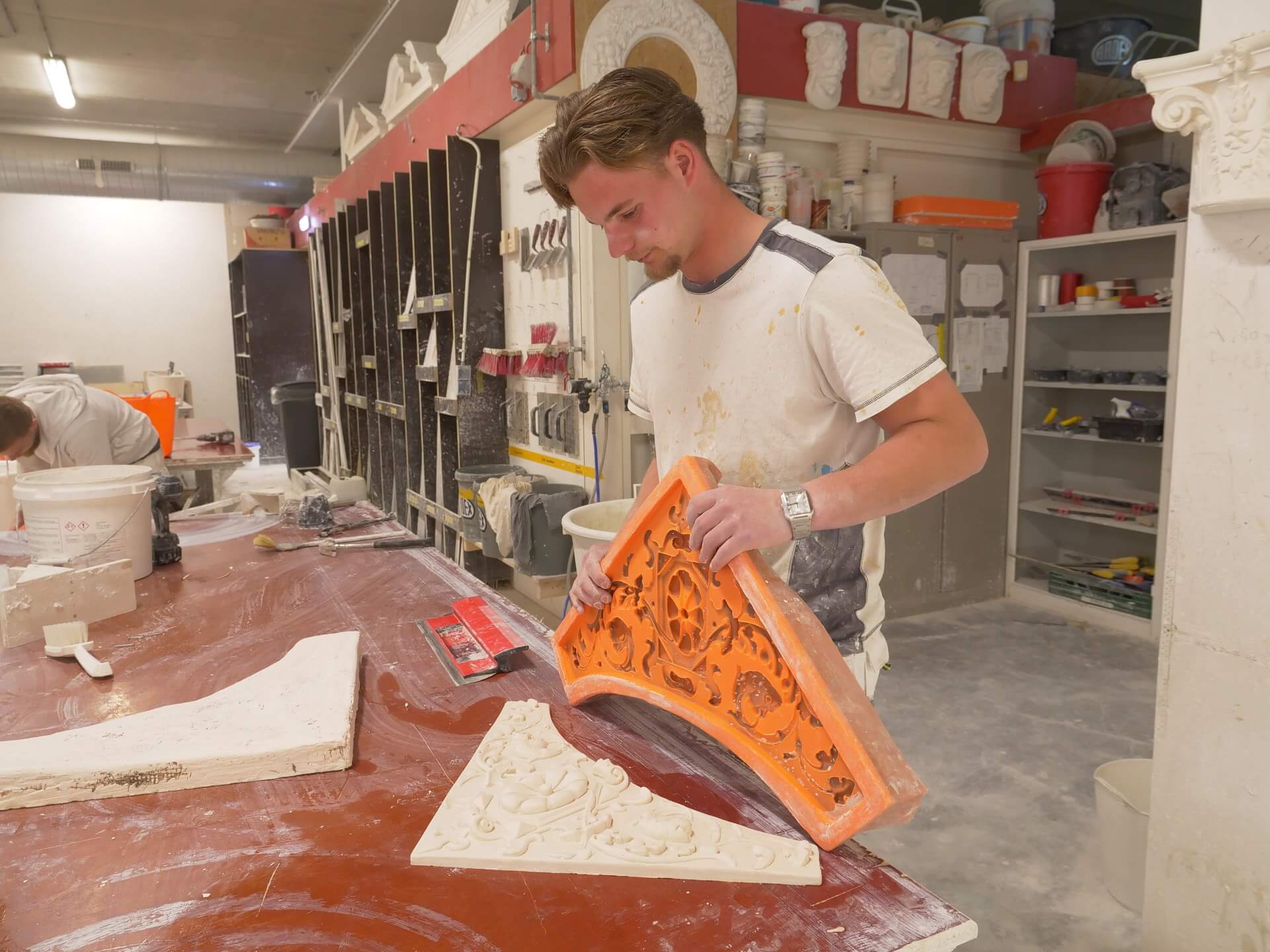 Student beeldhouwkunst werkt met een mal om decoratief stucwerk te maken in een praktijkruimte.