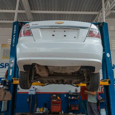 Technicus voert onderhoud uit aan een opgehangen personenauto in een werkplaats voor voertuigherstel.