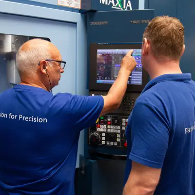 Twee technici bedienen een CNC-machine en bespreken de instellingen voor metaalbewerking.