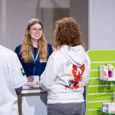 Medewerker informeert bezoekers over zorgproducten aan een balie in een zorggerichte omgeving