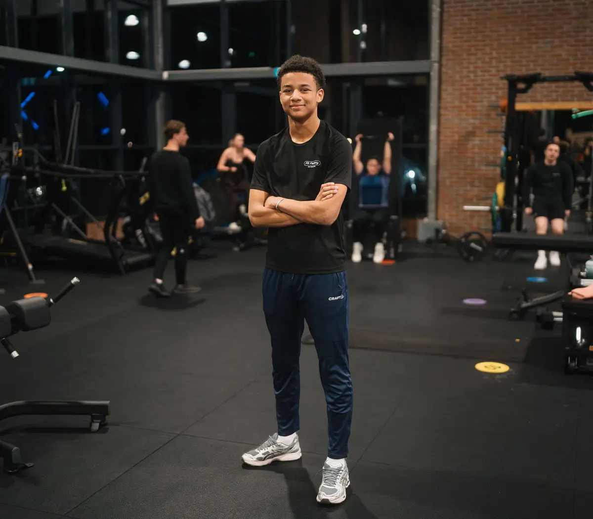 Sport- en bewegingsleider staat met armen over elkaar in een sportschool en begeleidt sportactiviteiten.