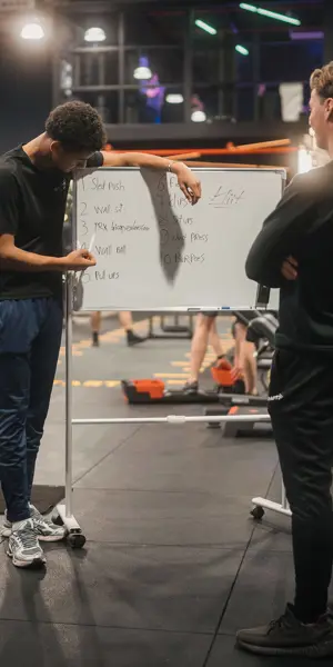 Sport- en bewegingsleider geeft uitleg aan groep jongeren in sportschool over trainingsschema en oefeningen