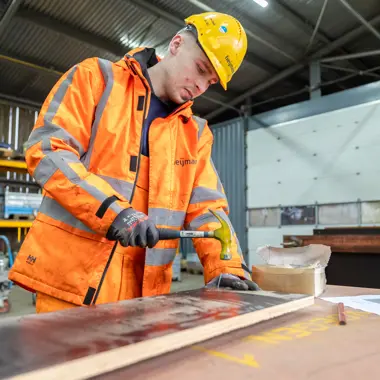 Vakbekwame medewerker werkt met gereedschap aan een houten oppervlak in een werkplaats voor infrastructuurprojecten