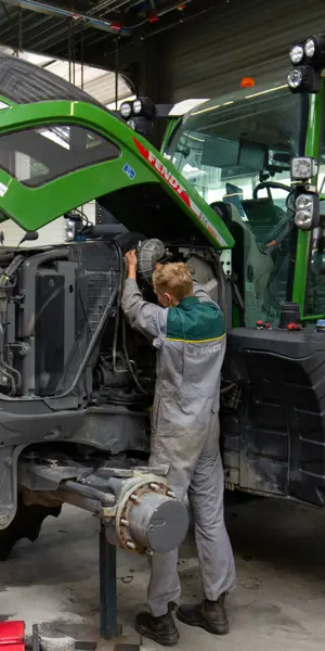 Technisch specialist onderzoekt de motor en systemen van een landbouwtractor in een werkplaatsomgeving