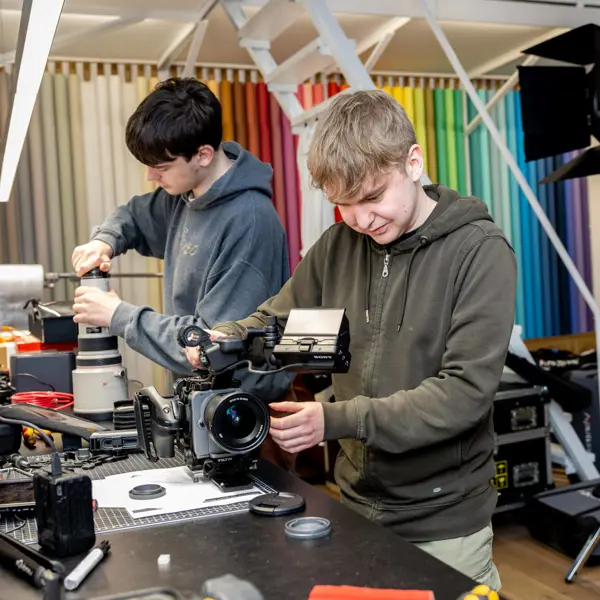 Twee studenten werken aan cameraapparatuur in een studioomgeving tijdens opleiding AV-specialist.
