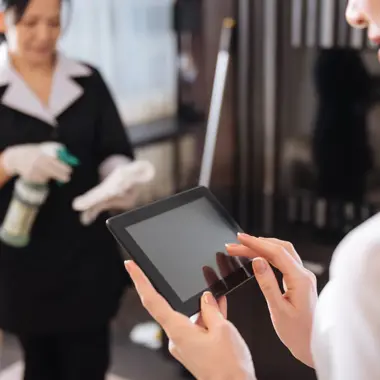 Schoonmaker bereidt zich voor terwijl begeleider instructies leest op tablet in een kantooromgeving