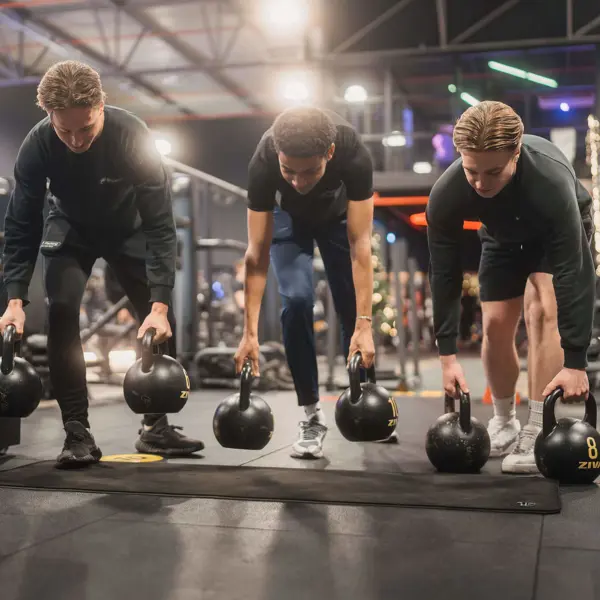 Drie sportbegeleiders oefenen kracht en coördinatie met kettlebells in een sportschool.