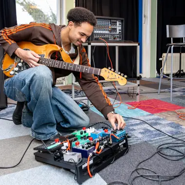 Student oefent met elektrische gitaar en geluidseffecten in een oefenruimte voor podiumtechniek.