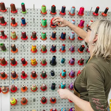 Persoon selecteert garen uit een wandrek, geschikt voor creatief vakmanschap en productontwikkeling.