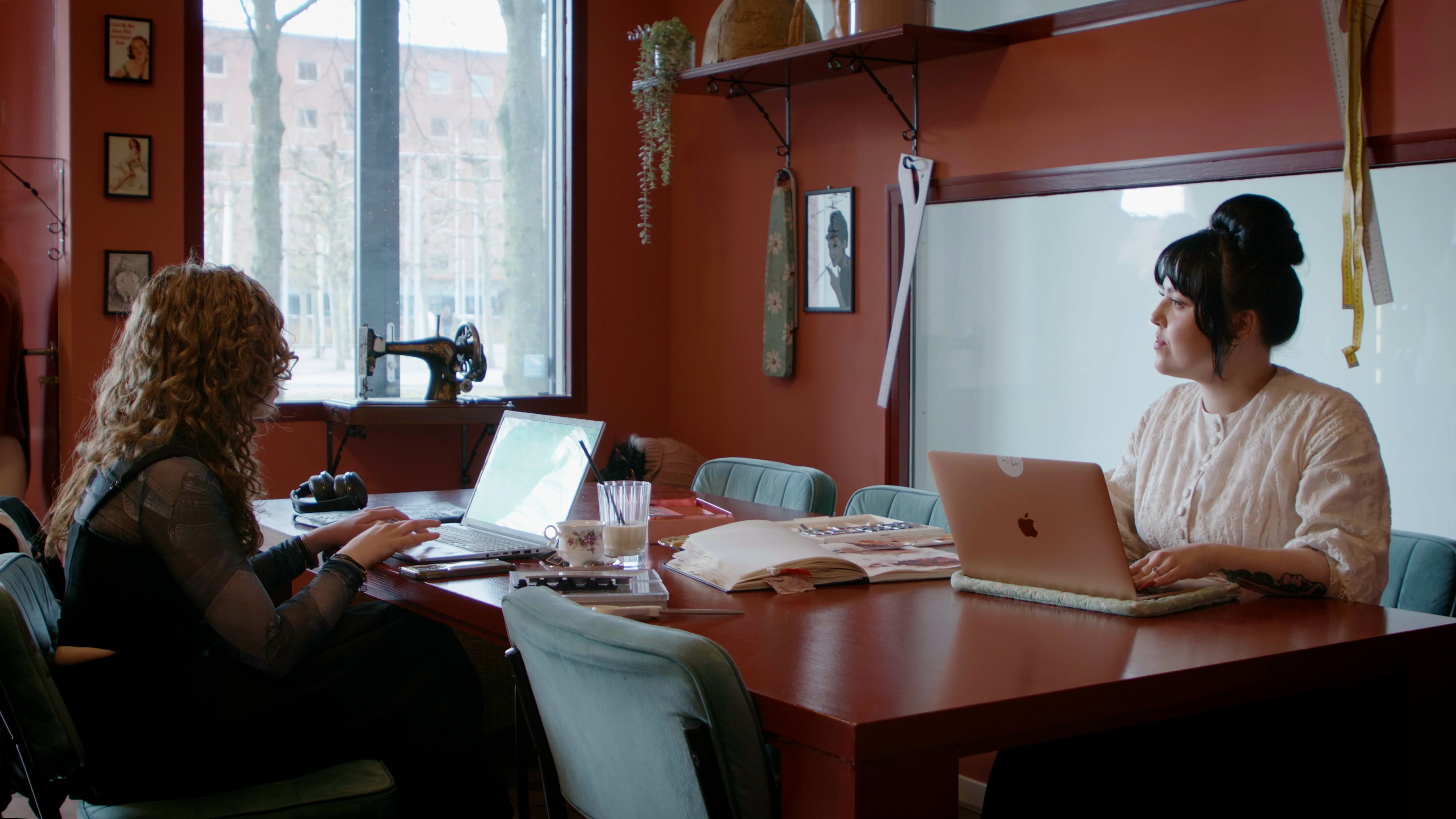 Twee studenten werken samen aan projecten met laptops aan een houten tafel in een studieruimte.