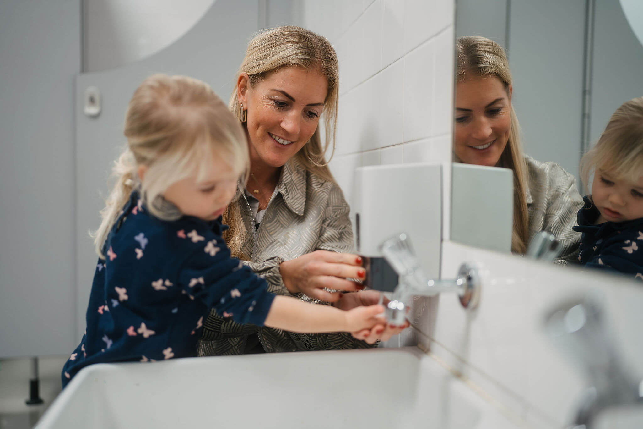 Begeleider helpt jongere met handen wassen aan wastafel in een leeromgeving