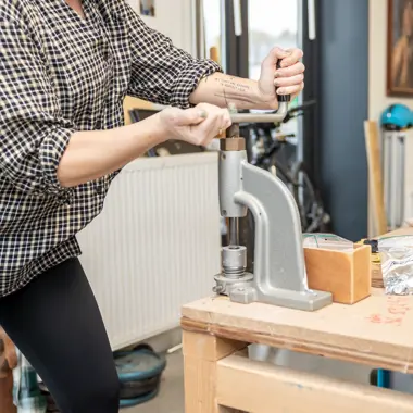 Persoon gebruikt een handpers om materialen te bewerken in een werkplaats voor hout en meubel.