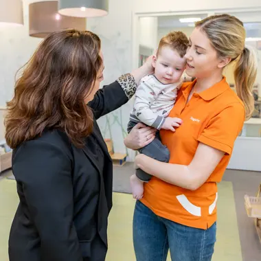 Medewerker in welzijn houdt jong kind vast terwijl bezoeker contact maakt, gericht op zorg en ondersteuning.
