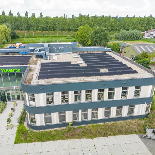 Groot schoolgebouw van Yuverta mbo Dordrecht met zonnepanelen op het dak, gezien vanuit de lucht.