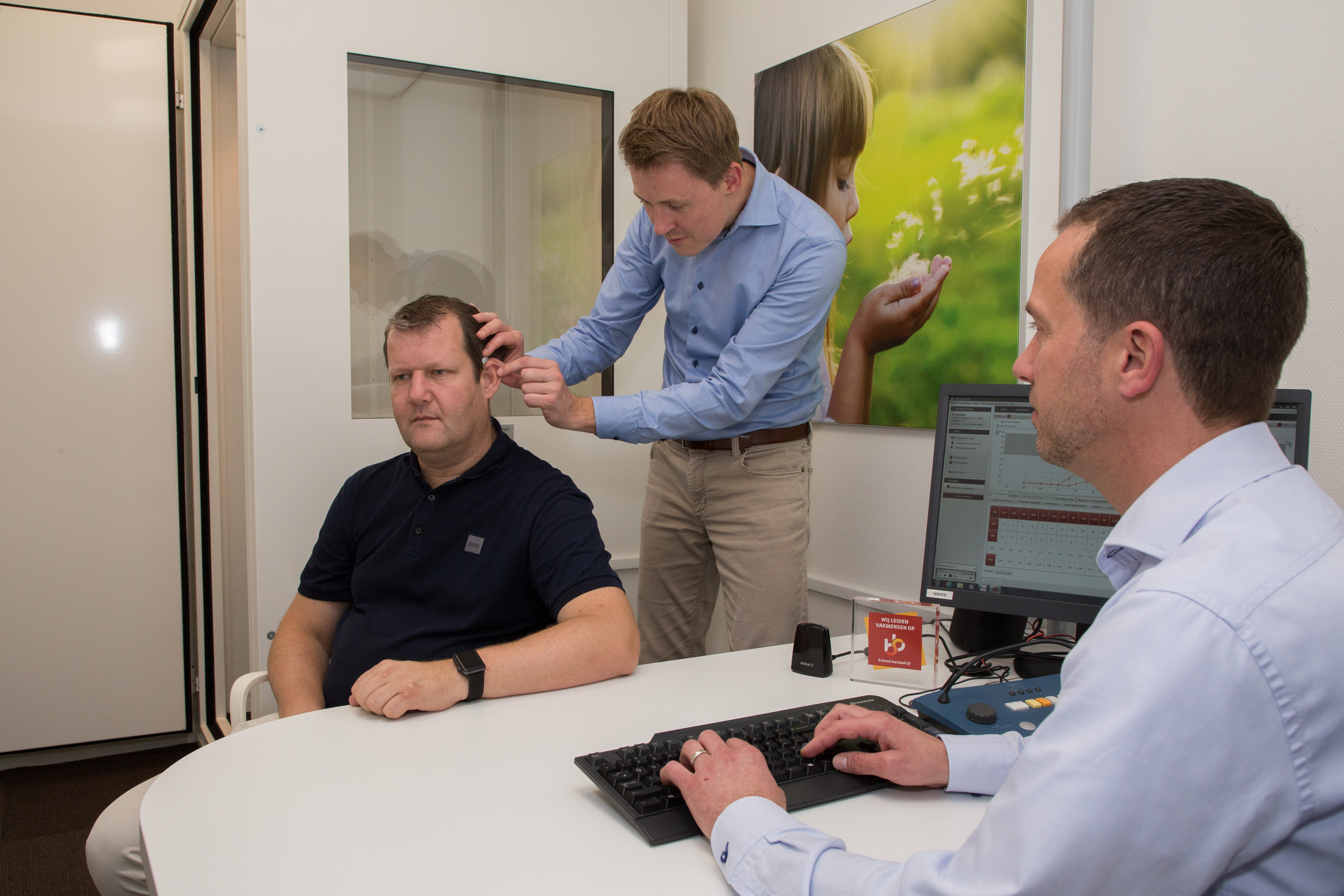 Audicien meet het gehoor van een klant terwijl collega een computer gebruikt voor analyse