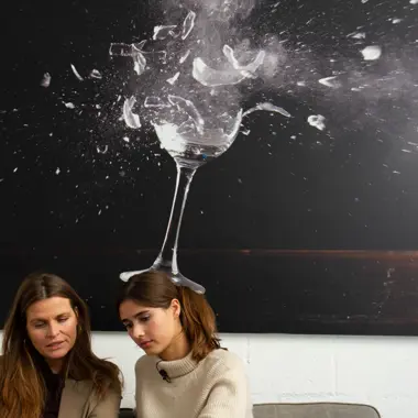 Twee personen werken samen aan een creatief project, met een kunstwerk van een brekend glas op de achtergrond