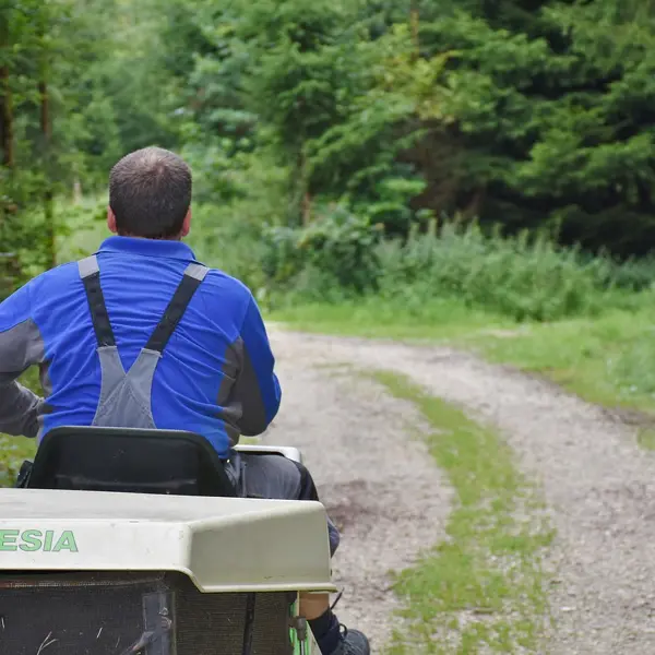 Beheerder die terrein onderhoudt met machine in een groene natuuromgeving.