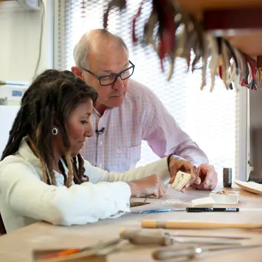 Docent begeleidt student bij het maken van een uniek sieraad in een creatieve werkruimte