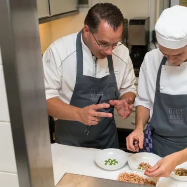 Gespecialiseerde kok begeleidt student bij het bereiden van een gerecht in professionele keuken
