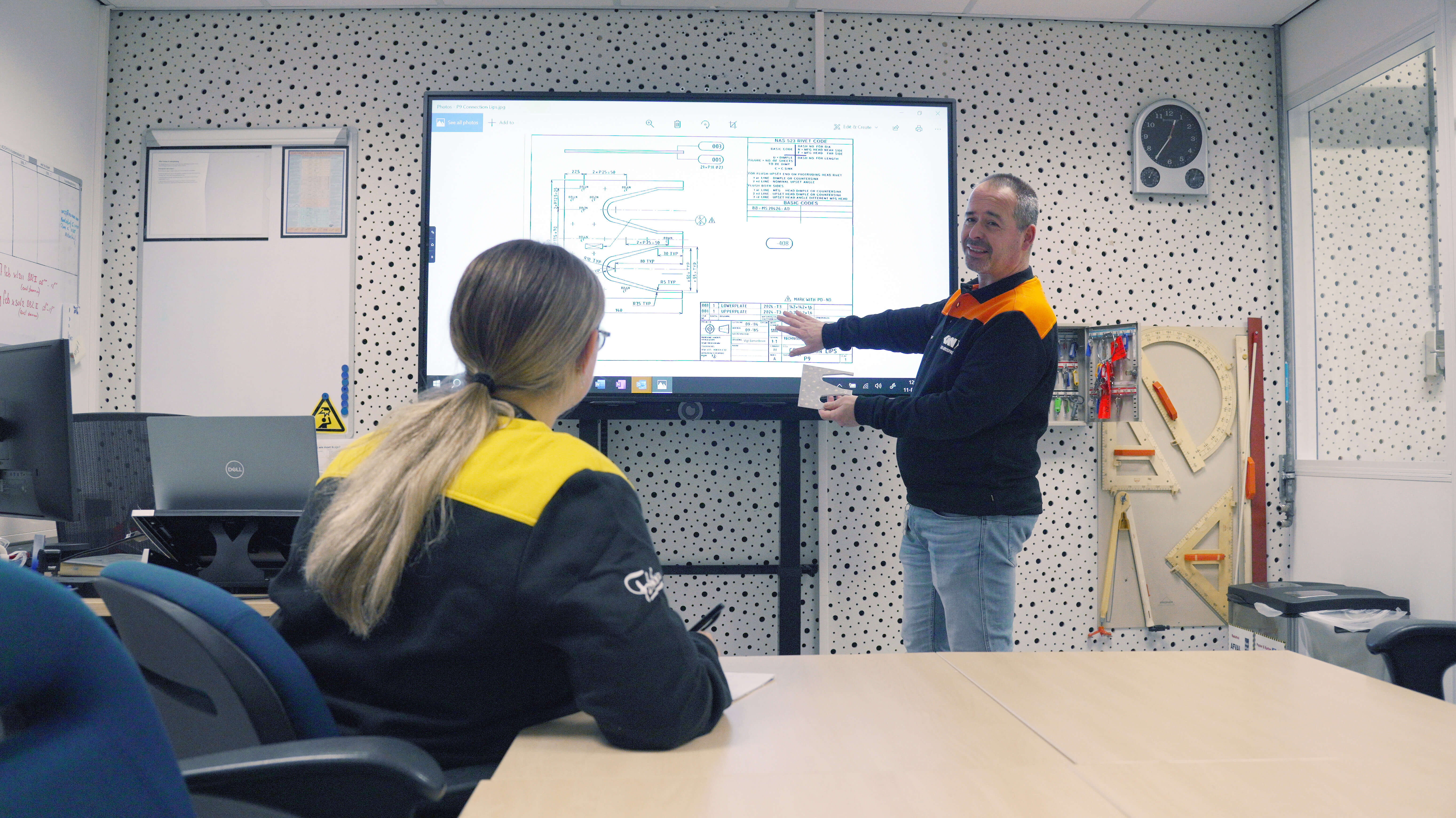 Docent legt technische tekening van vliegtuigonderdeel uit aan student in leslokaal