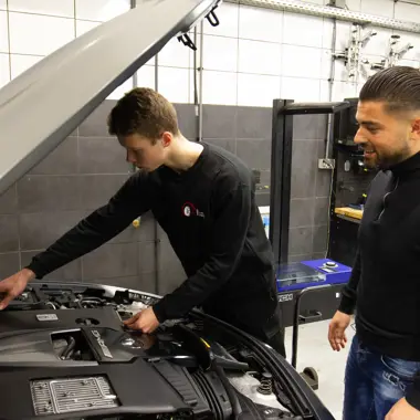 Student onderzoekt motorruimte van voertuig onder begeleiding van docent in technische werkplaats