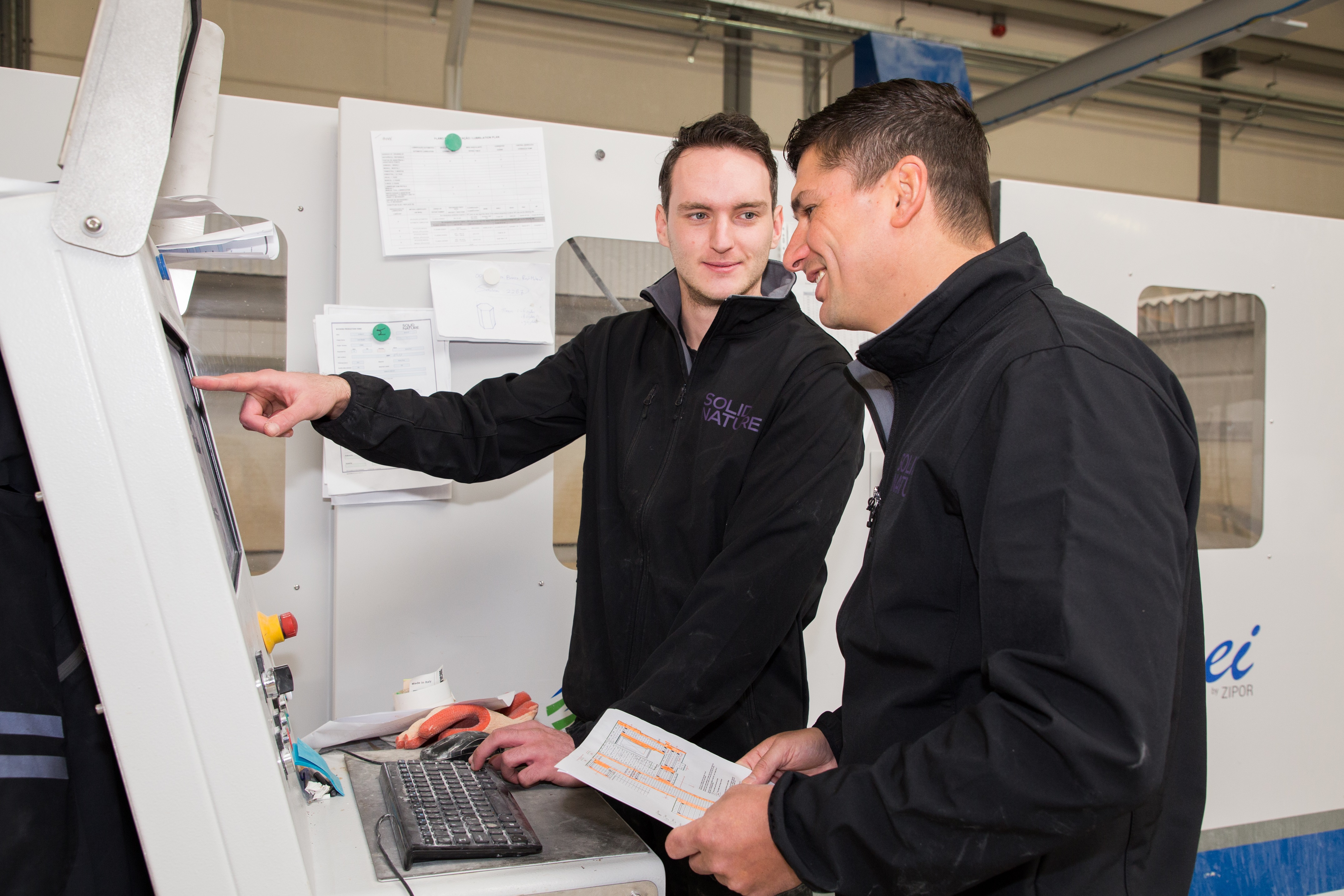 Twee medewerkers in een werkplaats bedienen samen een machine voor natuursteenbewerking.